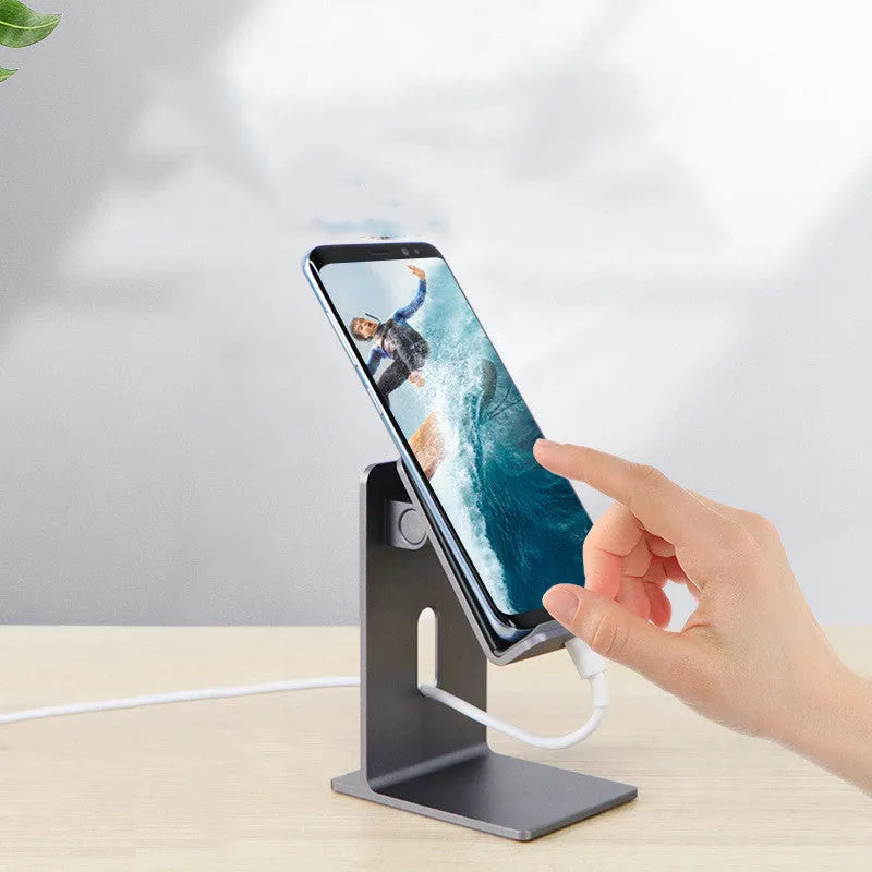 Dark grey alloy mobile phone and tablet holder with adjustable clamp on a wooden desk.