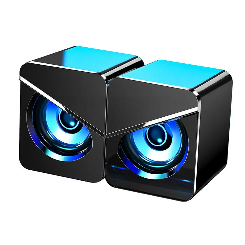 A pair of small black or white plastic desktop computer speakers with USB and 3.5mm audio cables.