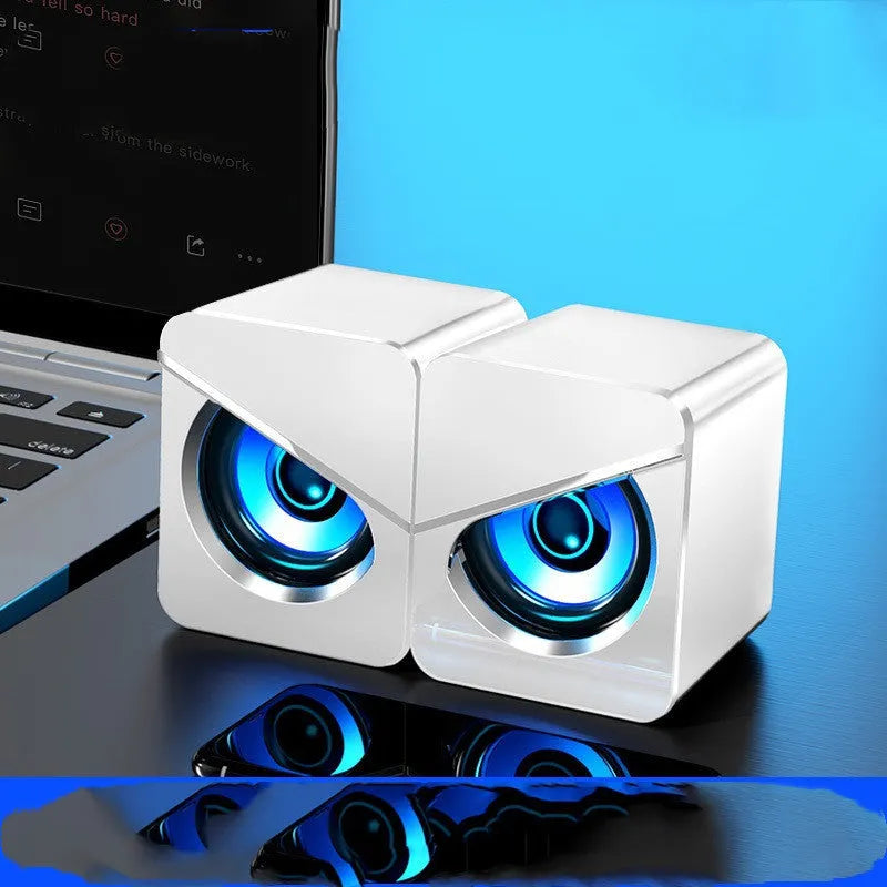 A pair of small black or white plastic desktop computer speakers with USB and 3.5mm audio cables.