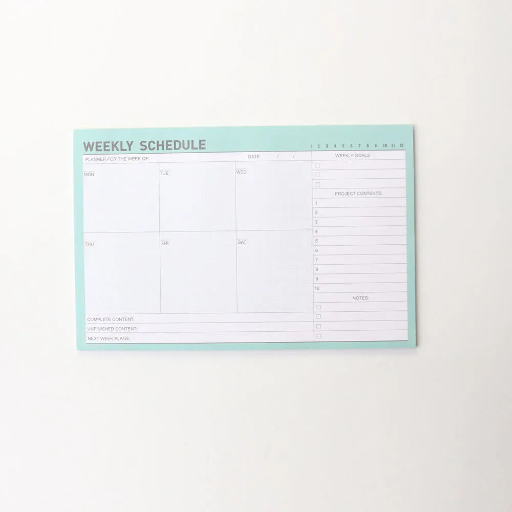 Domikee student desk organiser pad open to show weekly and monthly planning pages in pink and green.