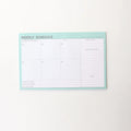 Domikee student desk organiser pad open to show weekly and monthly planning pages in pink and green.