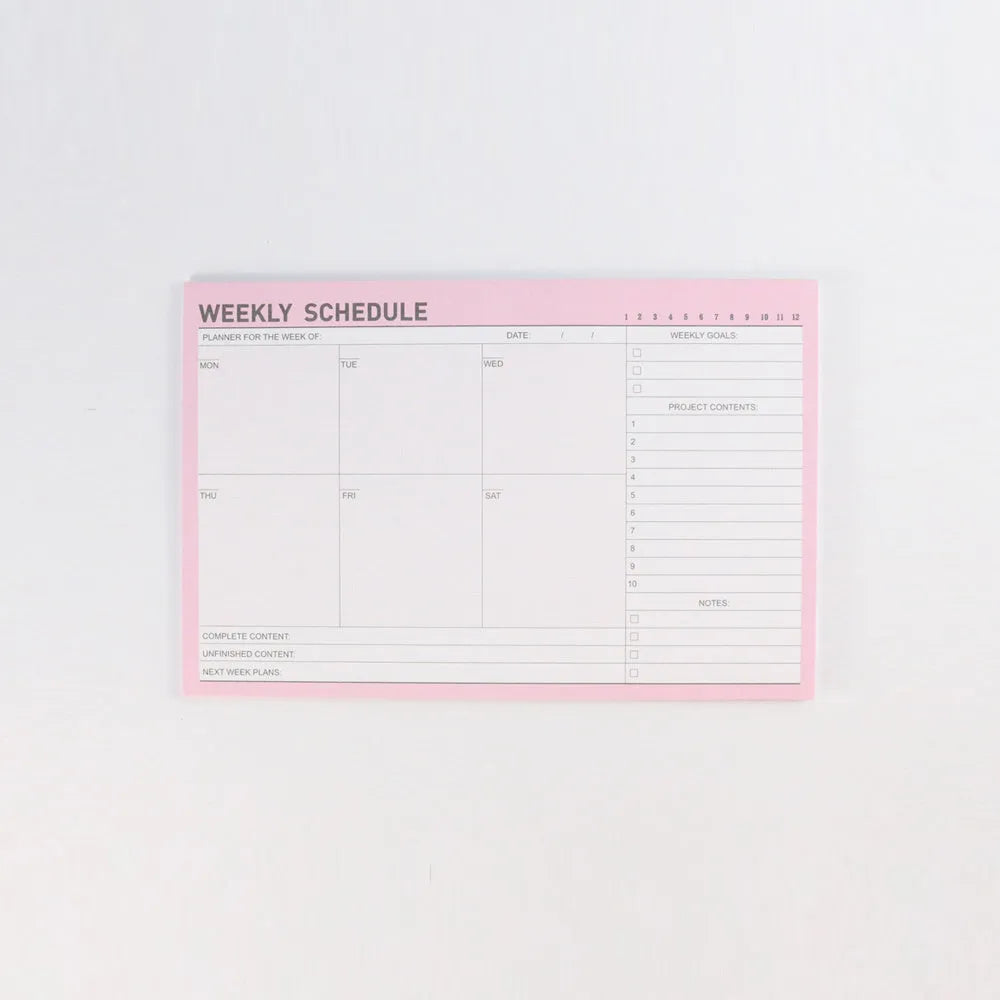 Domikee student desk organiser pad open to show weekly and monthly planning pages in pink and green.