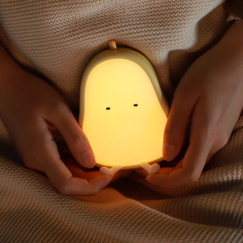 Soft white silicone pear-shaped night light with a warm yellow glow on a wooden surface.