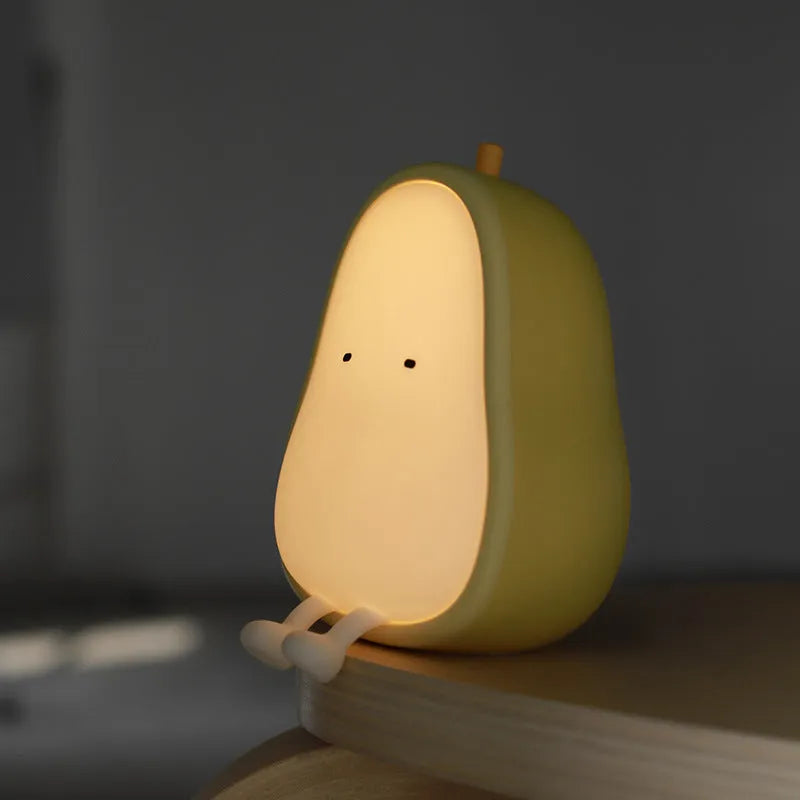Soft white silicone pear-shaped night light with a warm yellow glow on a wooden surface.