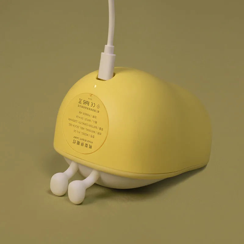 Soft white silicone pear-shaped night light with a warm yellow glow on a wooden surface.