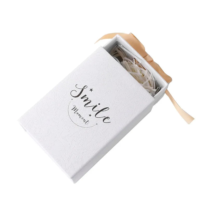 Small rigid cardboard gift box with bronzing detail, matching handbag, and raffia bow in four colour options.