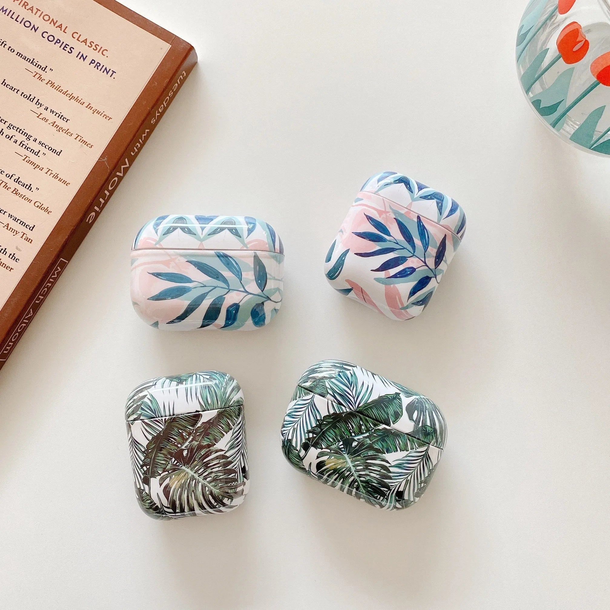 Blue and green TPU AirPods cases featuring a painted tropical banana leaf design.