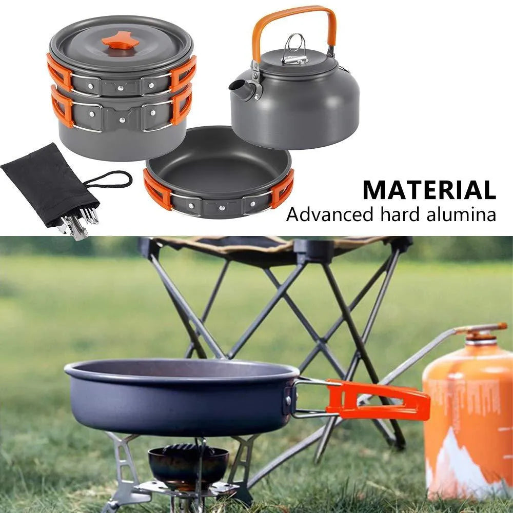 Orange folding camping cookware set with pots, pan, spoons, bowls in mesh bag on outdoor table