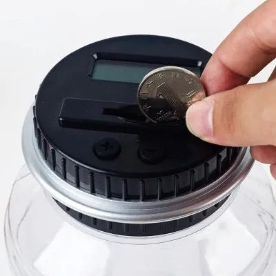Transparent digital coin counting money box with LCD screen on lid, showing coin slot and clear jar body