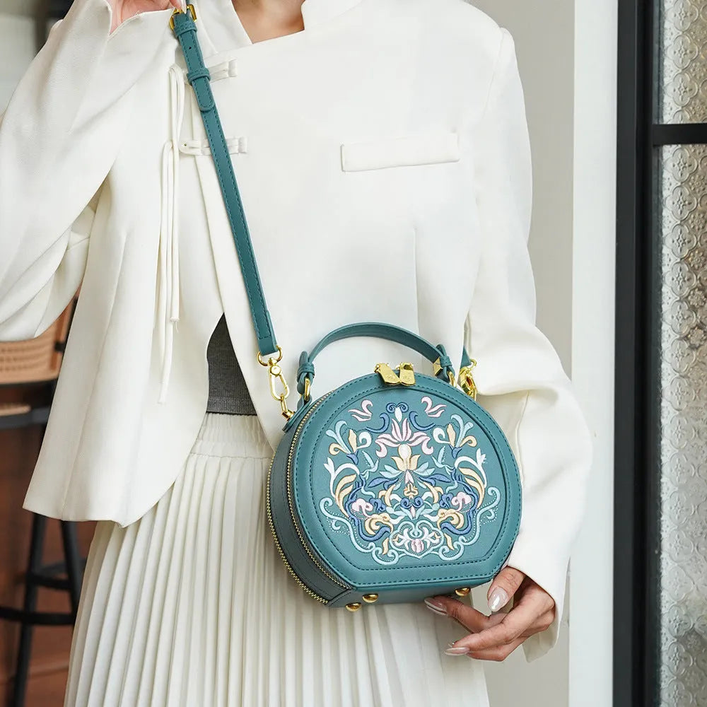 Small crossbody round bag in khaki with national-style embroidery and sewing line details, shown on a plain background