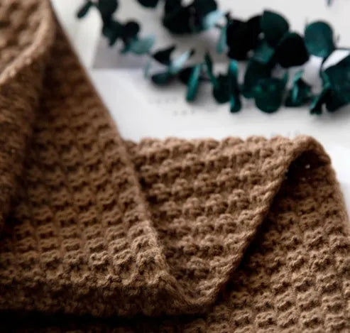 Nordic-style fringed knit acrylic blanket in a neutral colour, shown on a sofa.