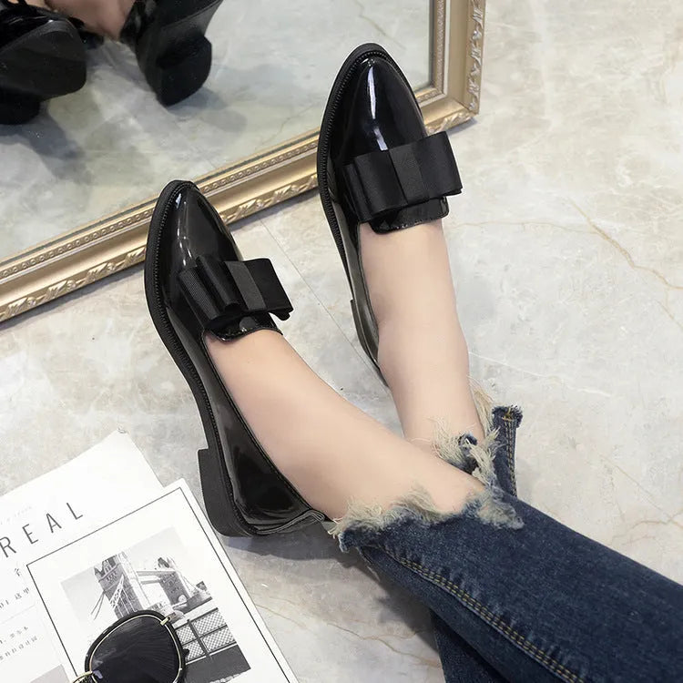 Women's patent leather pointed toe bowtie flats in black on a white background