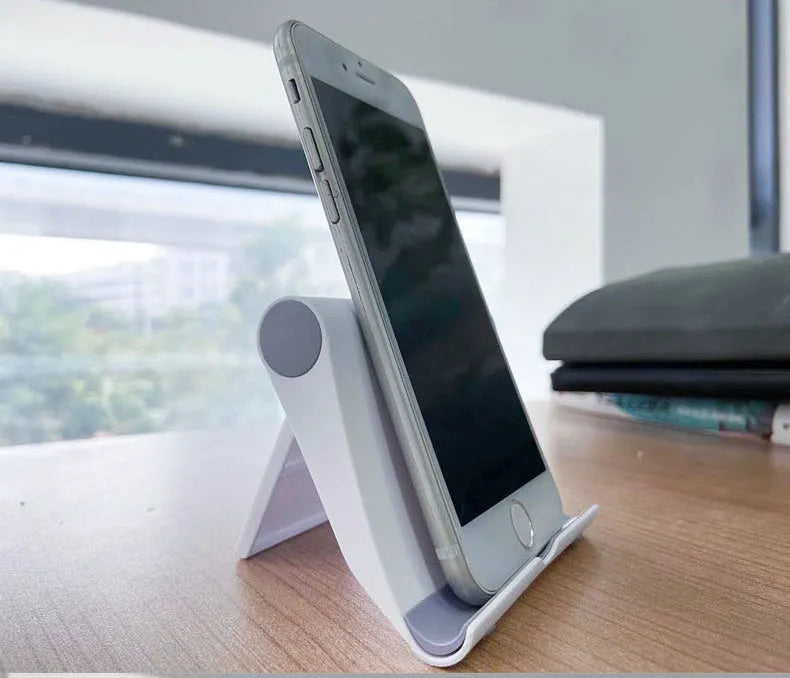 Black PE plastic folding stand holding a tablet at an adjustable angle on a wooden desk.