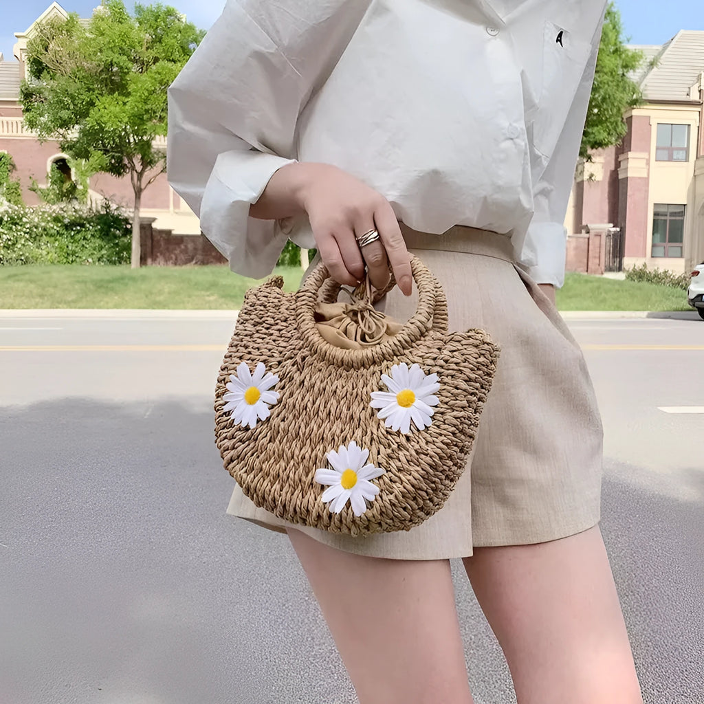 Light brown woven straw crossbody bag with daisy decoration showing shoulder strap