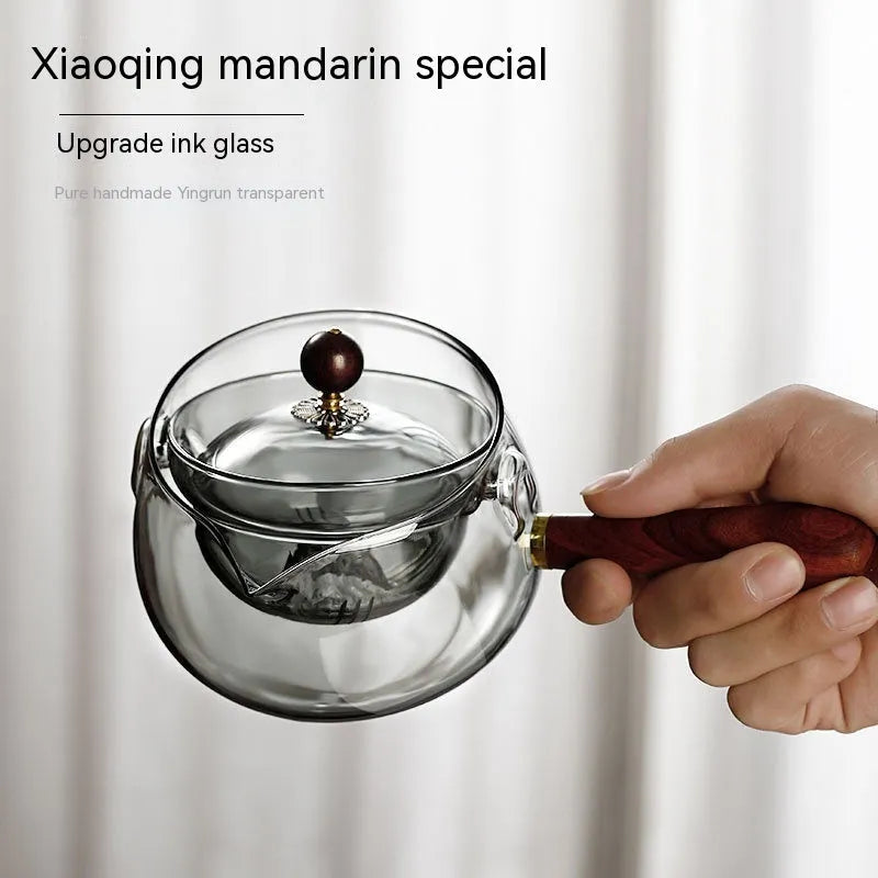 Transparent rotary glass teapot with wooden handle and built-in infuser on countertop