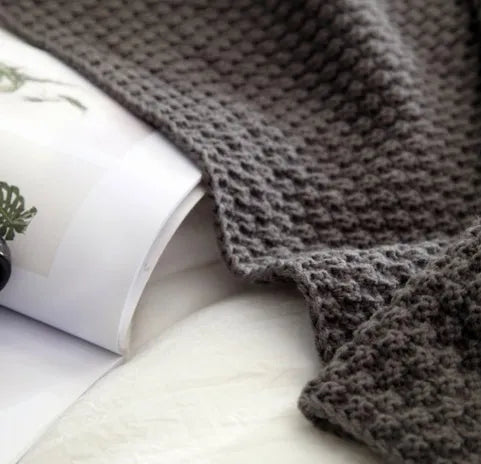 Nordic-style fringed knit acrylic blanket in a neutral colour, shown on a sofa.