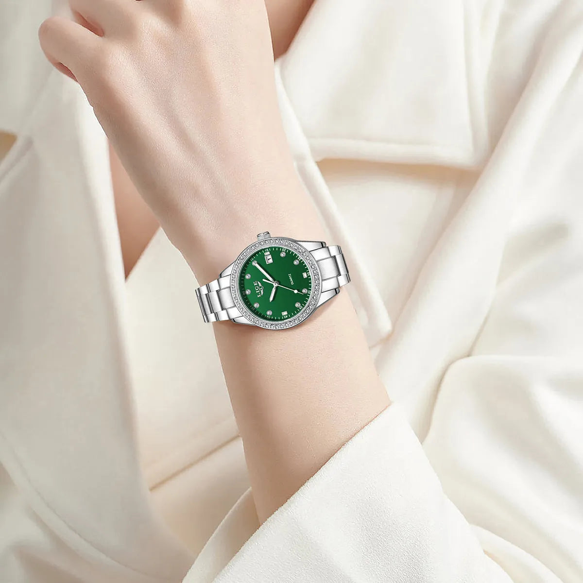 Women's silver and green quartz watch with diamond bezel, luminous hands, on a wrist.
