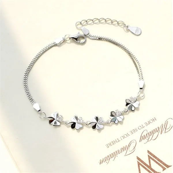 Silver four-leaf clover bracelet with leaf pendant on a plain background