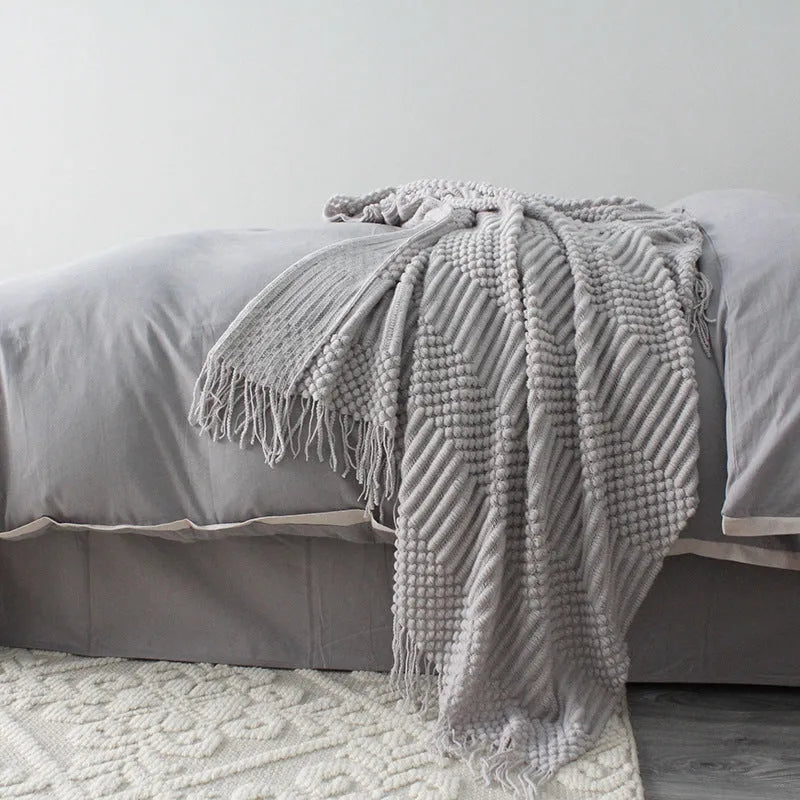 Small light grey polyester fleece throw blanket folded on a sofa.