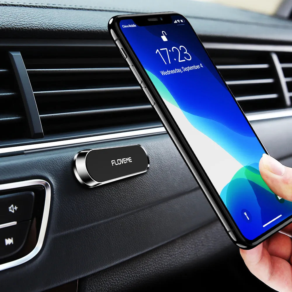 Black magnetic car phone holder with silver iron plate and white adhesive, shown next to a mobile phone.