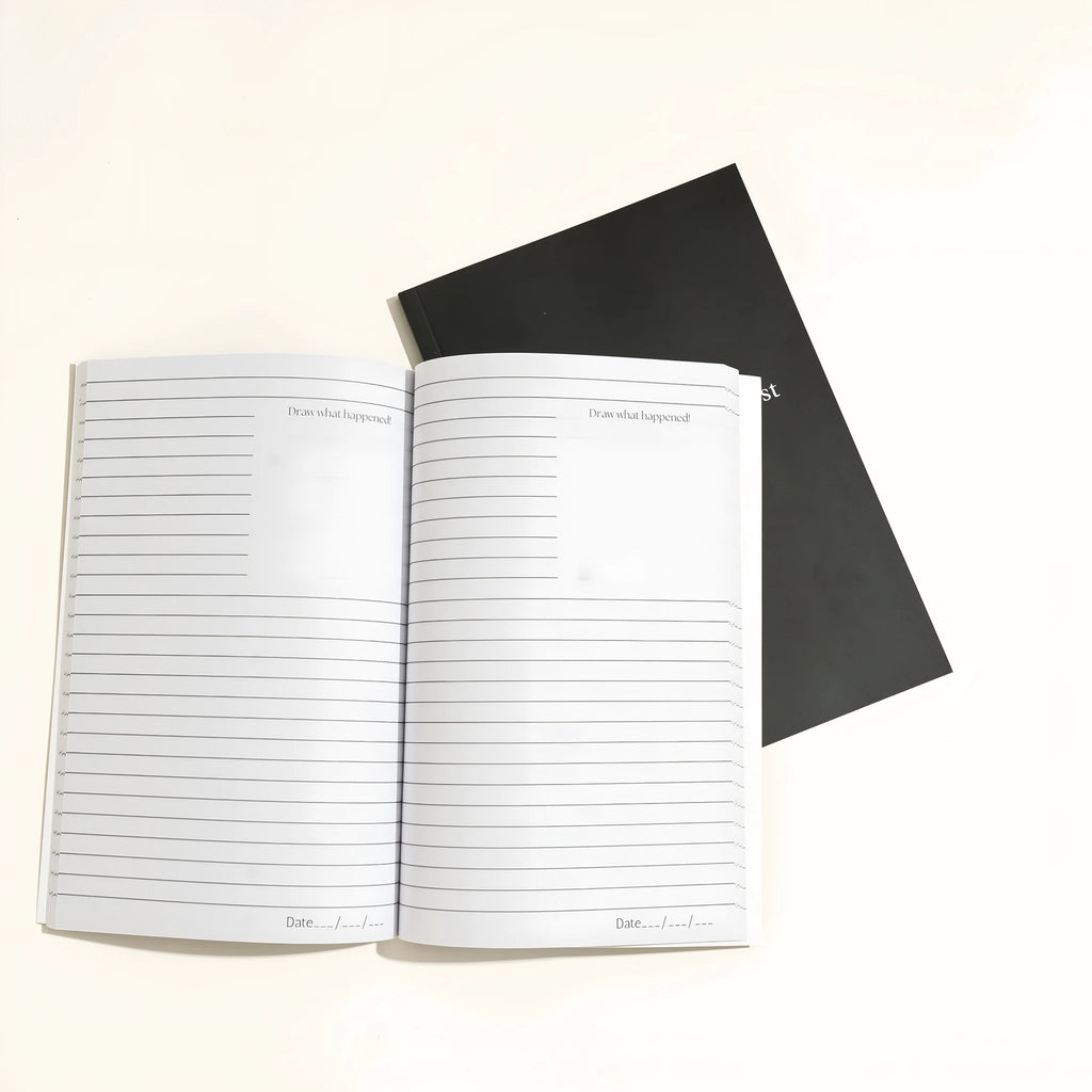 Black A5 hardcover dream journal with gold lettering, shown open on a lined page with a silk ribbon bookmark.