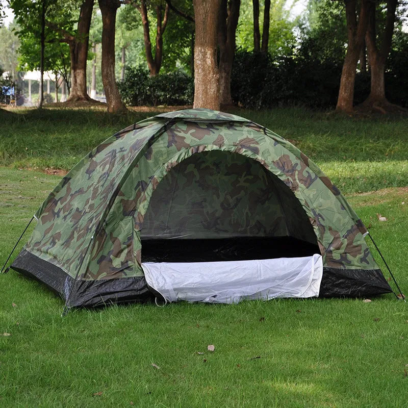 Green camouflage two-person camping tent with fibre glass poles and steel pegs pitched outdoors.