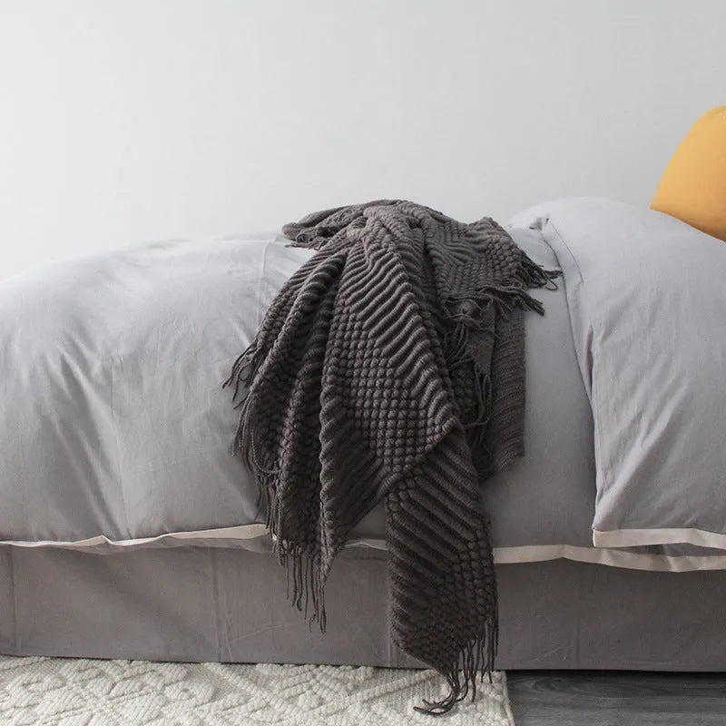 Small light grey polyester fleece throw blanket folded on a sofa.