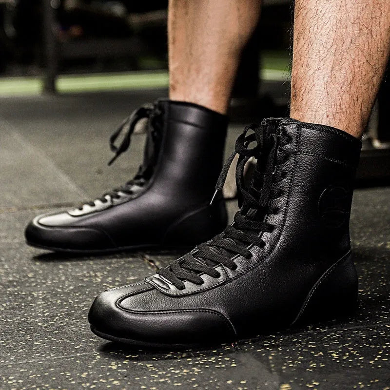 Pair of black and gold professional boxing shoes with mesh panels on a gym floor.
