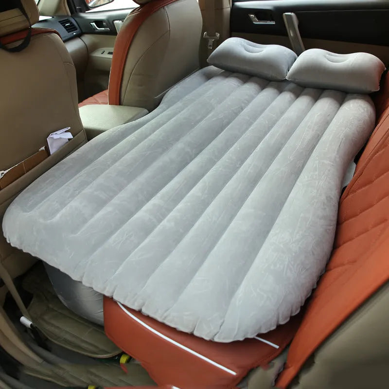 Black inflatable car bed with flocked material set up in the back of a five-seater vehicle, showing two pillows.