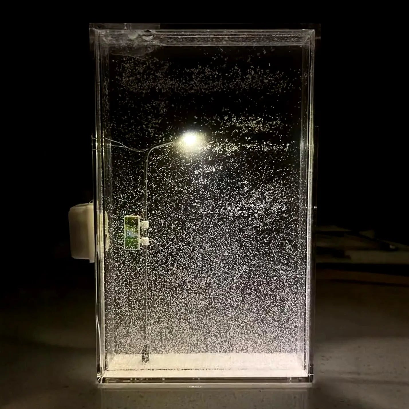 DIY snowy night light kit showing a small assembled street lamp with LED lights on a snowy flowing water landscape