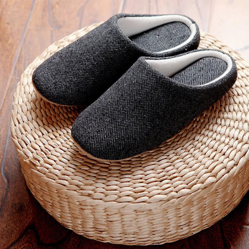 Men's black cotton indoor slippers with soft anti-skid sole on a wooden floor