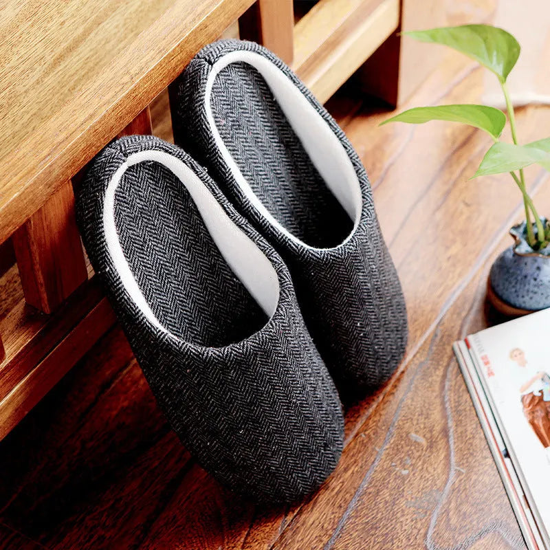 Men's black cotton indoor slippers with soft anti-skid sole on a wooden floor