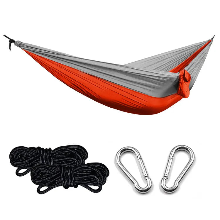 Ultralight outdoor camping nylon hammock in black grey colour, unfolded on grass with trees in background