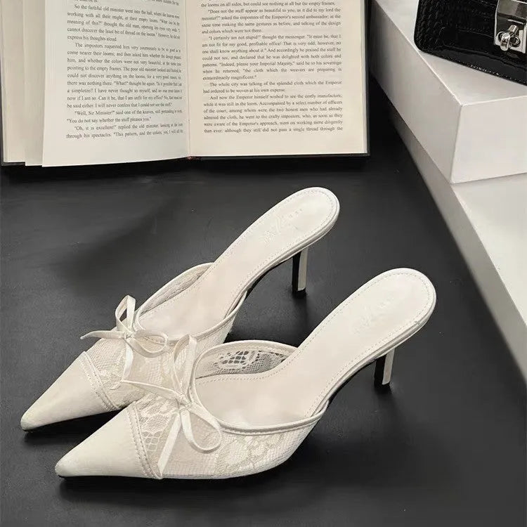 Women's light brown lace high heels with a pointed toe and a black bowknot detail on the front.