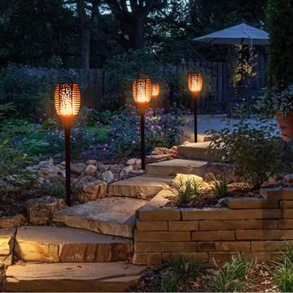 Solar-powered outdoor torch lights with vibrant LED displays automatically illuminating a garden pathway at night