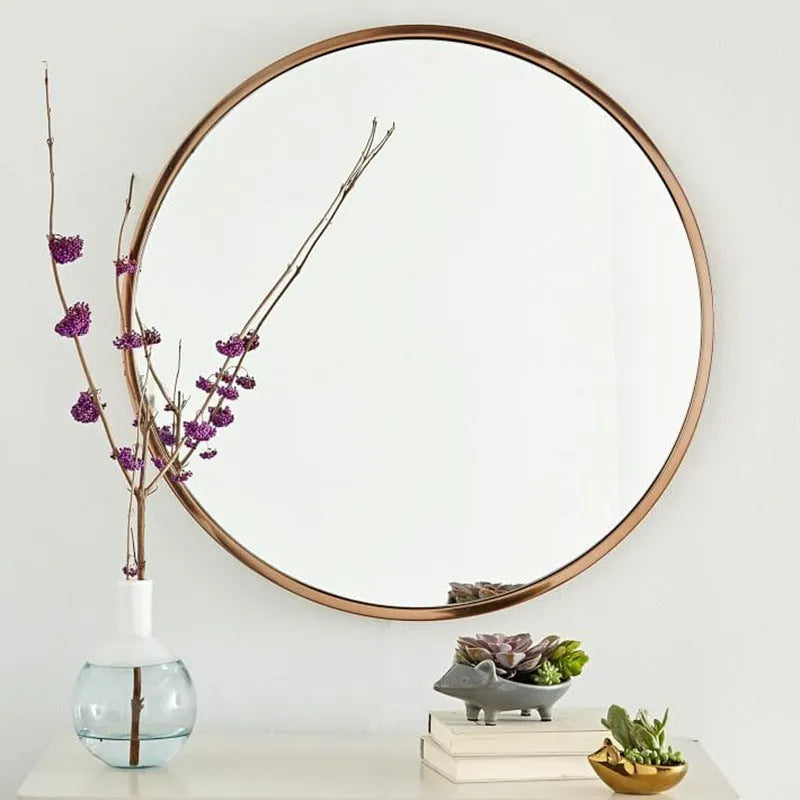 Round metal-framed wall mirror in black, white, or gold, shown in a bathroom setting.