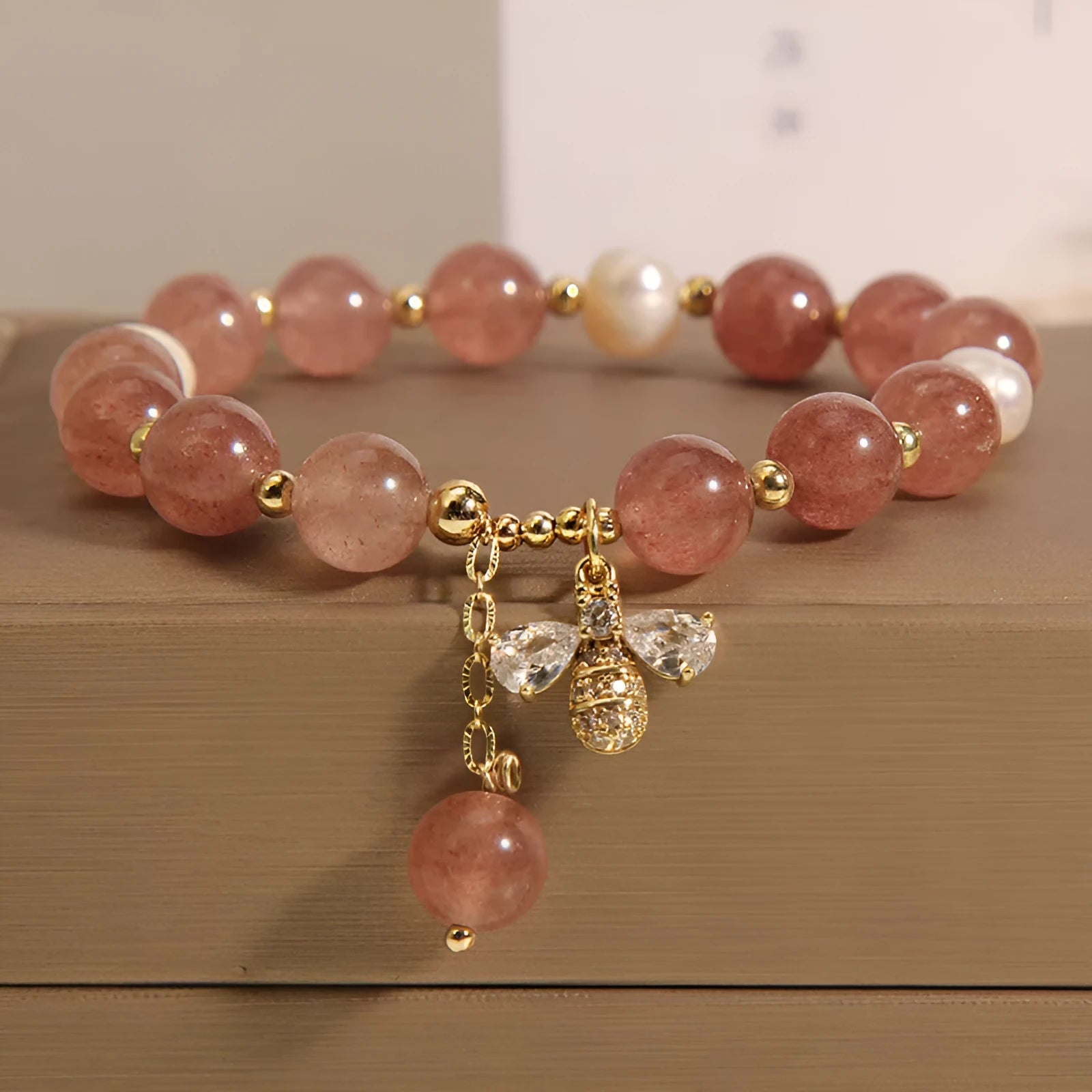 Close-up of a women's bracelet with pink strawberry quartz beads, white freshwater pearls, and sparkling zircon charms on an alloy chain.