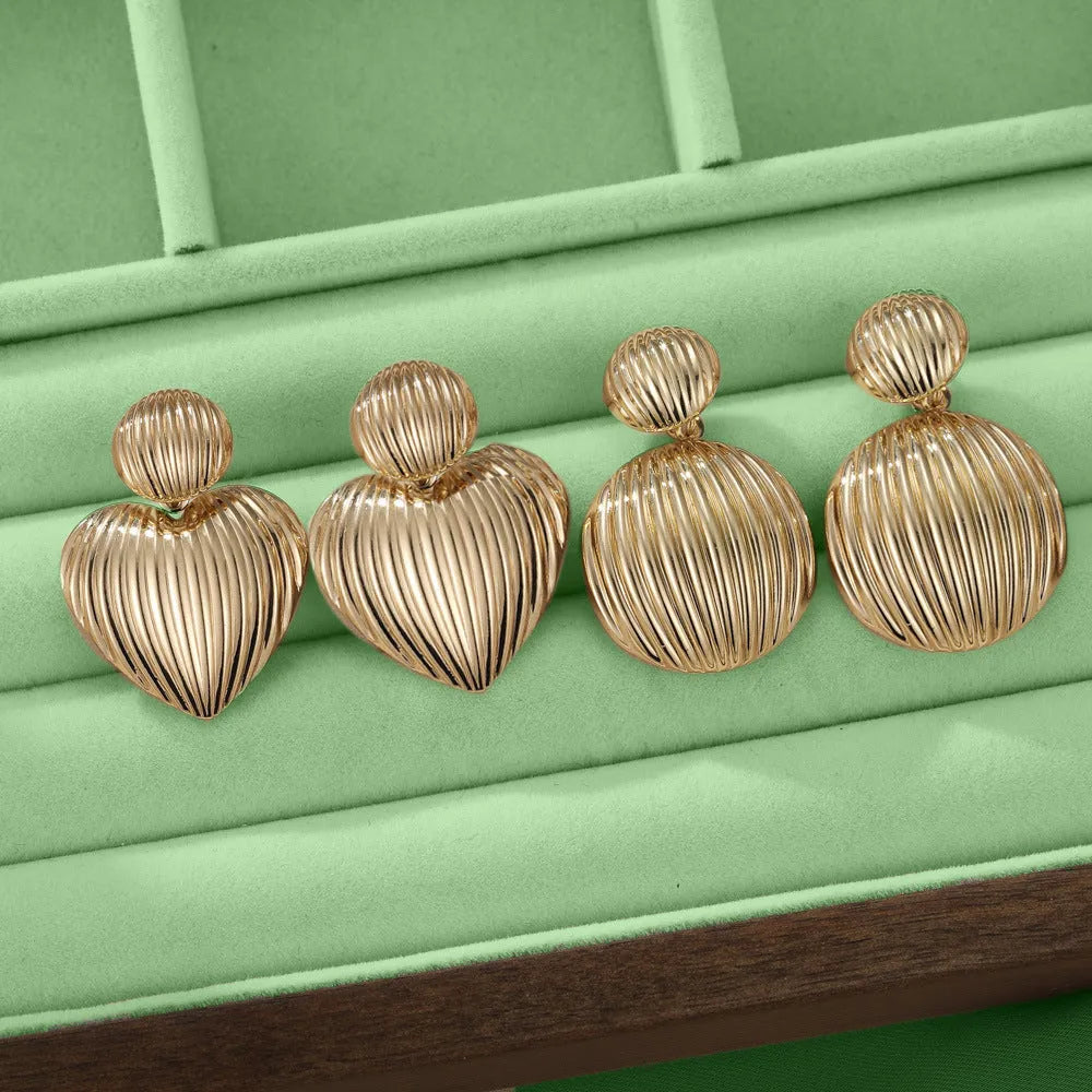 Gold alloy heart-shaped and round earrings for women on a plain background