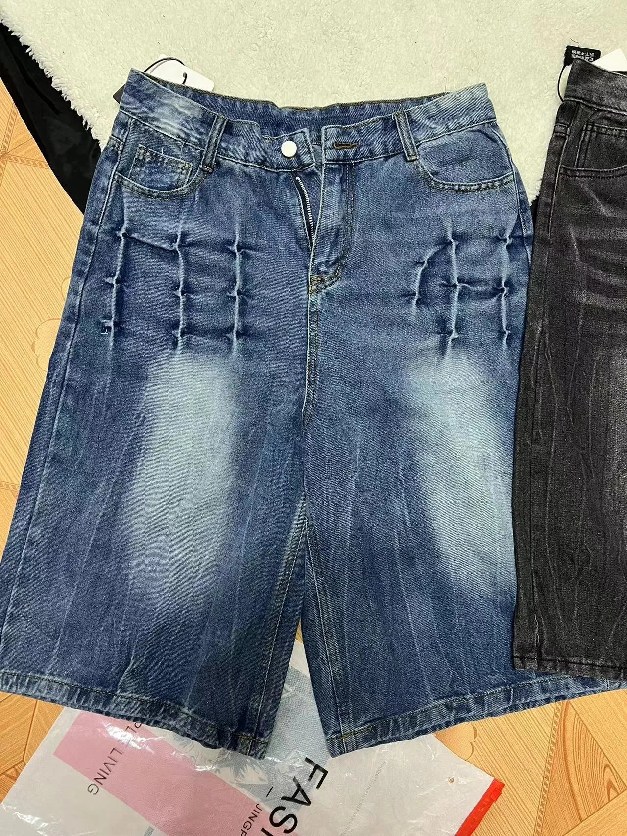 Man wearing loose straight-leg washed denim shorts in blue, showing cropped length and casual style.