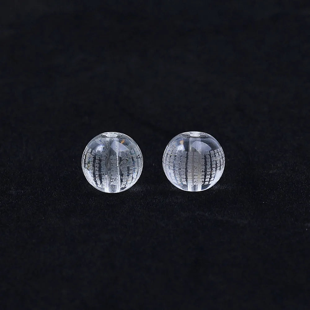 Ten 10mm round crystal prayer beads with Heart Sutra design, polished glass finish, scattered on a surface.