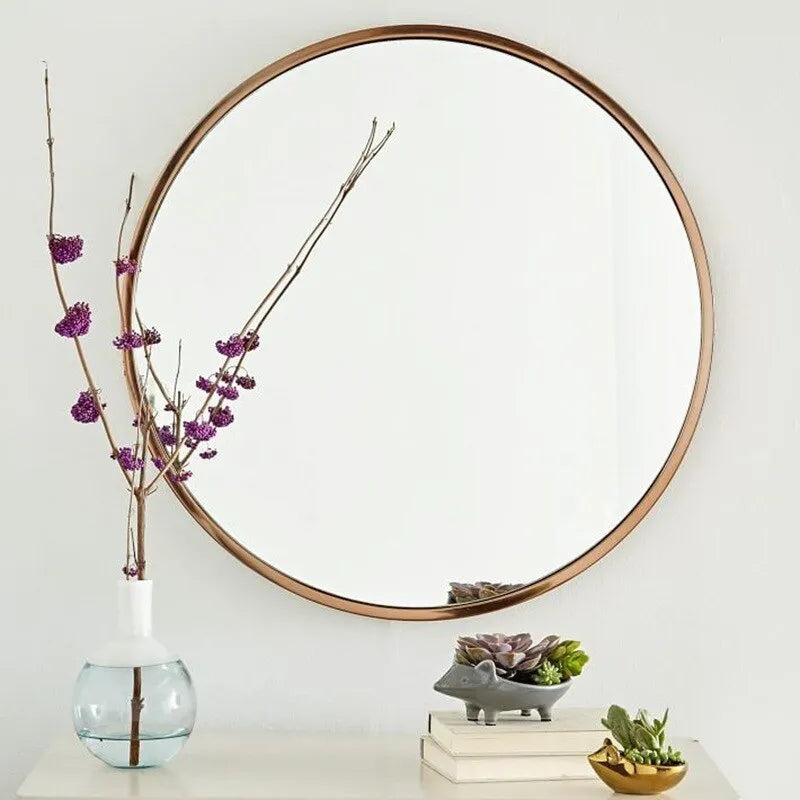 Round metal-framed wall mirror in black, white, or gold, shown in a bathroom setting.