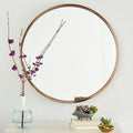 Round metal-framed wall mirror in black, white, or gold, shown in a bathroom setting.