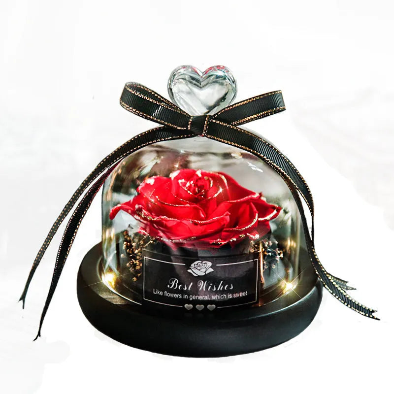 Eternal preserved red rose illuminated by LED light inside a clear glass dome on a wooden table.