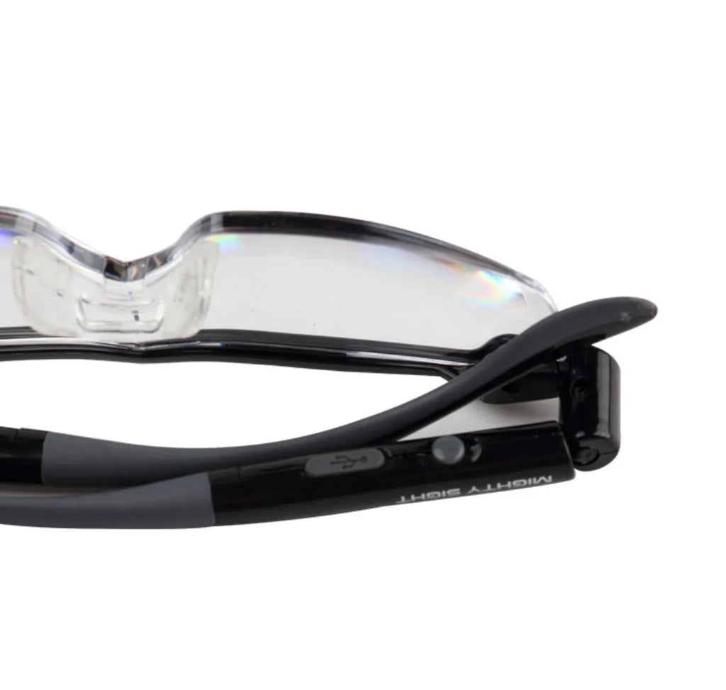 Transparent black USB LED reading glasses with ABS frame on a surface.