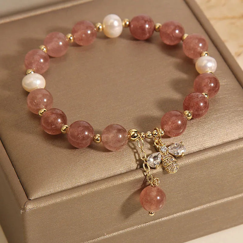 Close-up of a women's bracelet with pink strawberry quartz beads, white freshwater pearls, and sparkling zircon charms on an alloy chain.