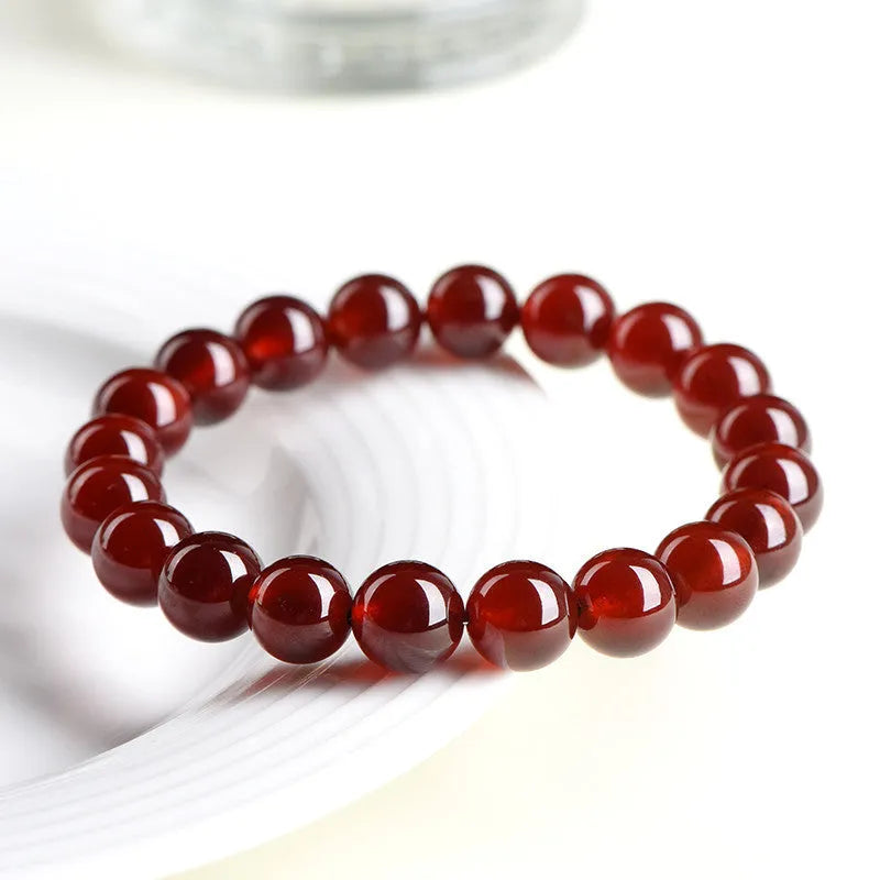 Natural orange red garnet ball crystal bracelet with a silver ruyi charm on a white background.