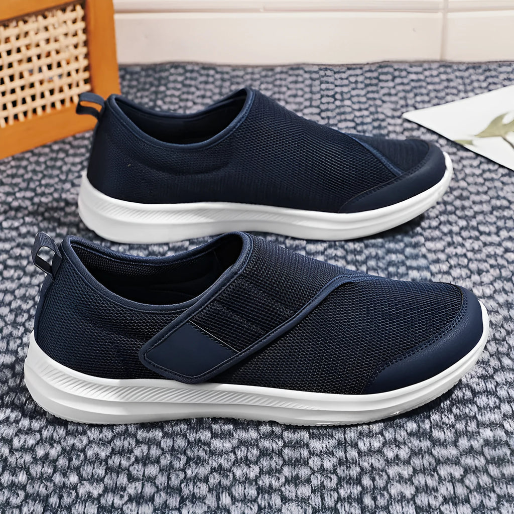 A pair of grey Velcro walking shoes with a mesh upper and round toe, shown on a white background.