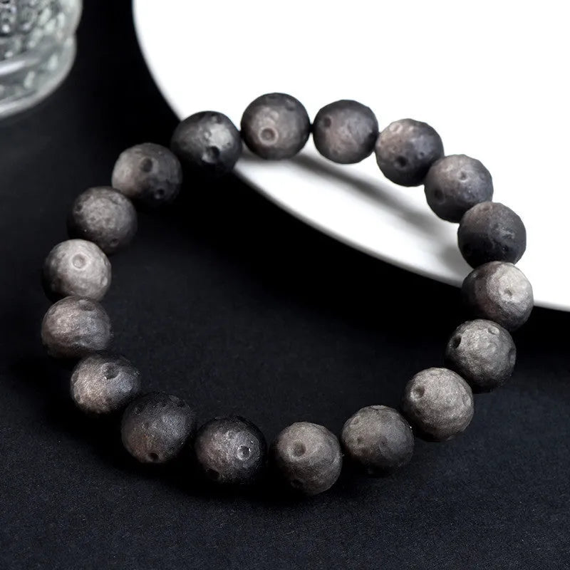 Natural obsidian crater ball bracelet with a ground texture in silver stone or gold colours on a wrist.