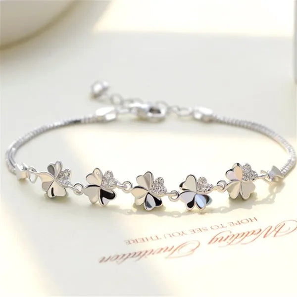 Silver four-leaf clover bracelet with leaf pendant on a plain background
