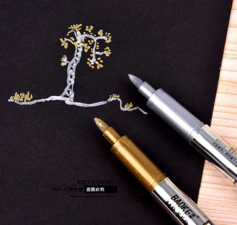 Gold and silver metallic marker pen set with dual tips lying on a white surface